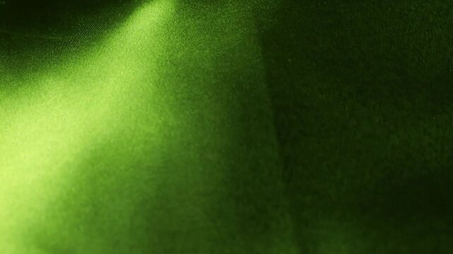Natural silk fabric in green shades develops in the wind creating abstract waves. Soft lighting emphasizes the smooth texture and flowing movement of the material. Dark olive and lime colors.