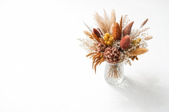 Aerial shot of a lone crystal vase filled with vivid dried floral arrangement and generous white background for copy space