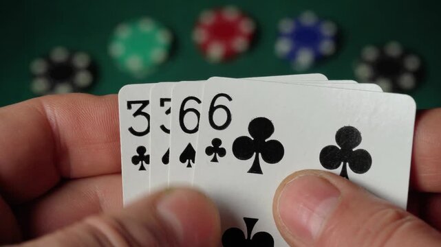 A player holds playing cards in his hand, including two pairs, and in the background, colorful poker chips are scattered on a green felt table