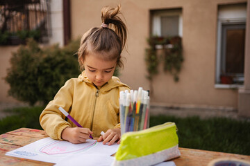 Young girl drawing on paper with marker pens outdoor © Jelena
