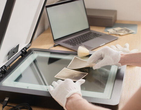 Hands carefully arrange old photos on a scanner bed. A person digitizes vintage paper prints, preserving history. Modern technology captures past images for a digital archive.