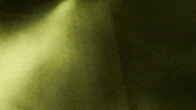 Abstract yellow silk fabric waving in the wind. Smooth natural textile creating flowing waves and golden highlights. Rippled surface of soft material with subtle dark patterns. 
