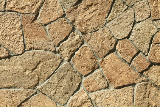 Granite stone wall, background, texture. Chaotic masonry surface of big granite rocks terracotta color. The wall texture of brown volcanic stones. Modern fashionable design for fences and barriers