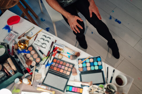 Drag queen preparing for performance, creating a glamorous look with colorful makeup, brushes, and eyelashes