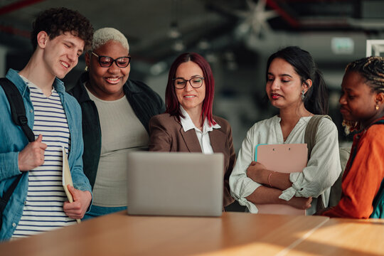 Diverse group of multi ethnic students and a female teacher gathering around a laptop, working on a project and learning together