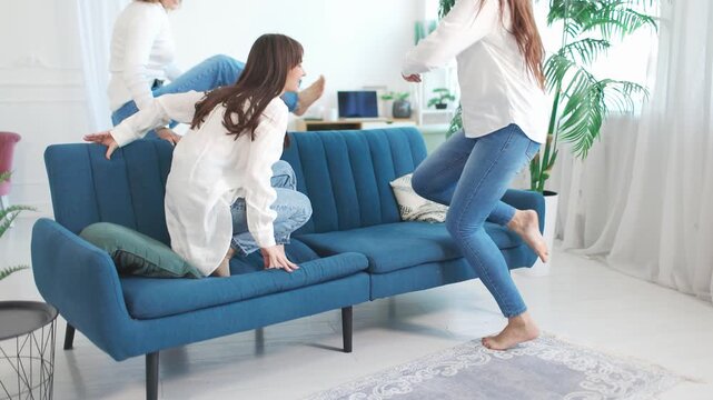 Pretty female friends jumping on sofa.