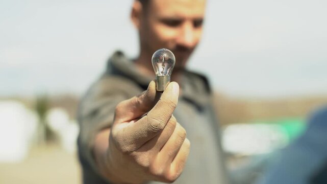 Close-up of a man's hand holding a burned-out car light bulb