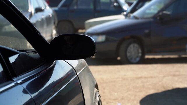 Car side mirror in a parking lot with blurred vehicles in the background on a sunny day, urban transport concept.