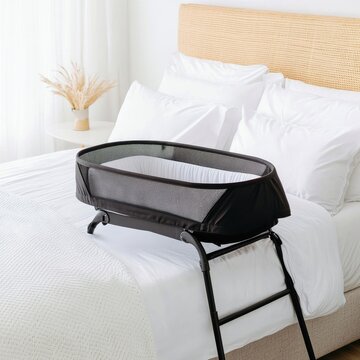 Modern black mesh bedside baby bassinet on a pristine white bed with rattan headboard, promoting safe infant sleep and stylish minimalist nursery integration. Co-sleeper, Newborn