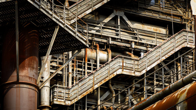 Close up of industrial steel structure with stairs pipes and platforms, heavy industry architecture with rusted metal surfaces and complex engineering detail