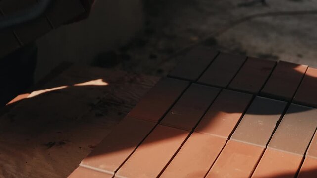 Worker carrying bricks from stack with arranged rows on floor close up