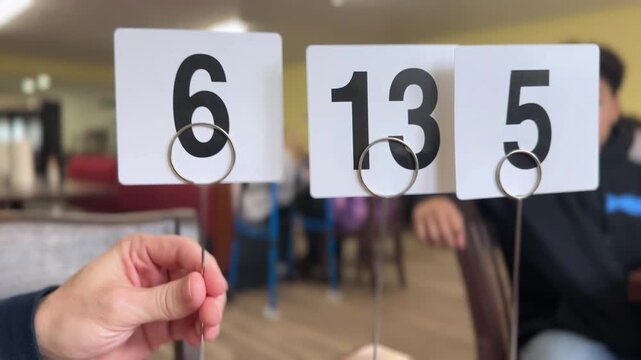Hand placing numbered table markers at a restaurant, showing order numbers for food service pickup and table identification in a casual dining setting. 15121