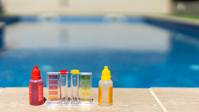 Close-up of a pool water testing kit with reagent bottles and color comparator, used for measuring pH and chlorine levels in a backyard swimming pool - pool maintenance concept