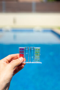 Close-up of a hand holding a pool water testing kit with color scale, measuring pH and chlorine levels in a clear blue swimming pool outdoors - pool maintenance concept