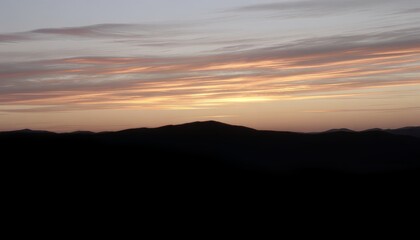 Obraz premium The sun sets behind a mountain range casting a warm orange glow on the clouds in the evening sky