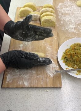 : Close-up of a chef in black gloves stuffing potato dough with fried cabbage to make traditional Zrazy. Cooking process on a wooden board sprinkled with flour.