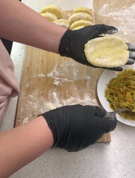  Close-up of a chef in black gloves stuffing potato dough with fried cabbage to make traditional Zrazy. Cooking process on a wooden board sprinkled with flour.