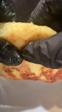 Close-up of a chef in black nitrile gloves breaking a crispy fried patty (zrazy) to reveal the hot filling inside: golden saut&eacute;ed cabbage with carrots and green dill. Appetizing food demonstration.