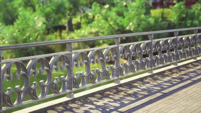 Ornate iron railing casting long shadows across cobblestone path, decorative scrollwork in sharp focus, soft bokeh trees in background, warm golden light,