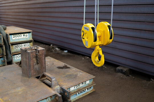 Yellow overhead crane hook suspended above heavy metal counterweights with marked capacities inside industrial facility showing lifting equipment and load handling system