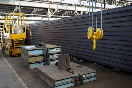 Wide view of industrial warehouse with suspended crane hook, metal counterweights and lifting machinery showing large scale material handling and heavy equipment operations