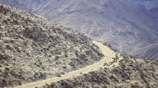 Historicfeel switchback trail winding across dry hillside, india highland corridor evoking old trade and caravan routes, layered terrain, weathered soil,