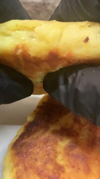 Close-up of a chef in black nitrile gloves breaking a crispy fried patty (zrazy) to reveal the hot filling inside: golden saut&eacute;ed cabbage with carrots and green dill. Appetizing food demonstration.