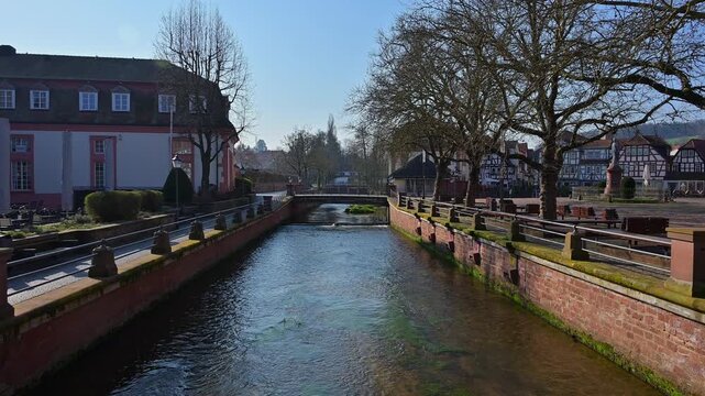 Fluss flie&szlig;t zwischen B&auml;umen und historischen Geb&auml;uden unter blauem Fr&uuml;hlingshimmel, Fluss M&uuml;mling, Erbach, Odenwald, Hessen, Deutschland