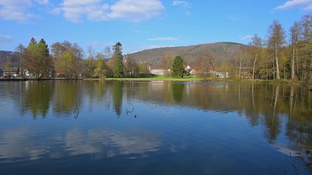 See spiegelt den blauen Himmel und die umliegenden B&auml;ume wider, Seegarten, Amorbach, Odenwald, Bayern, Deutschland