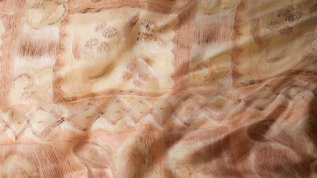 Natural silk fabric with beige and brown geometric patterns waving in the wind. Abstract background of moving soft waves and organic drapes. Elegant textile surface with decorative prints.