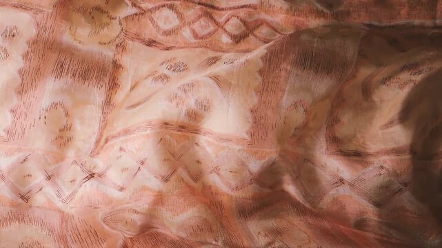 Silk fabric with abstract geometric patterns waving in the wind creating soft ripples. Natural textile material with ethnic brown and beige ornaments moving in slow motion. Abstract background.