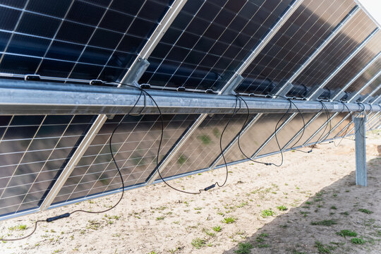Technical detail of the underside of photovoltaic modules featuring black cables and galvanised support racks for sustainable electricity generation and clean tech infrastructure