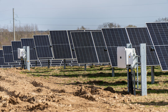 Wide rows of industrial solar panels with electrical inverter boxes on tracker systems in a rural field for renewable energy production and sustainable power grid development