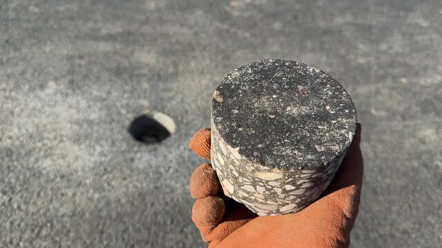 Slow motion 4K, worker holding an asphalt core sample taken from a road surface, with a drilled hole visible