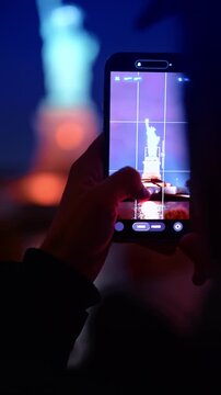 New York, USA, 2 April 2026: Person taking photo of Statue of Liberty with smartphone night. Close up of hand holding smartphone screen displaying Statue of Liberty photography at night.
