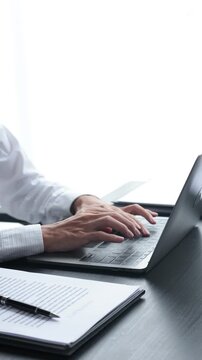 Businessman typing on laptop with signed contract on office desk.