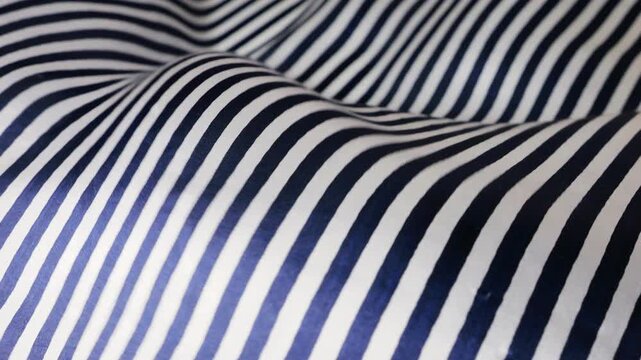 Blue and white striped natural silk fabric waving in the wind. Abstract background of moving soft waves and curves. Elegant textile with vertical lines pattern fluttering outdoors.
