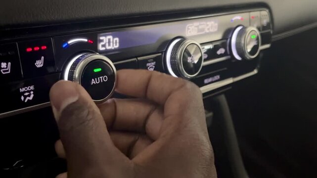 Hand adjusting climate control dial on modern car dashboard