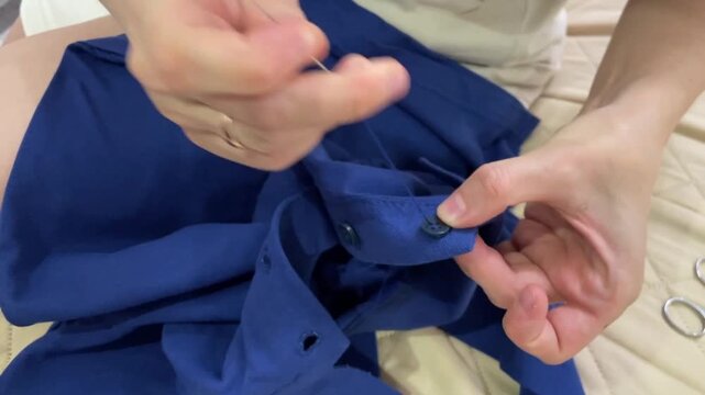 Woman mending clothing, Repairing navy jacket with care, Woman meticulously sewing cuff button on navy garment, Detailed focus on handwork restoring vintage style cuff button on clothing