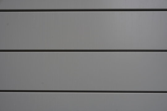 Close-up of modern architectural cladding featuring horizontal grey metal panels with clean, dark recessed shadow gaps.