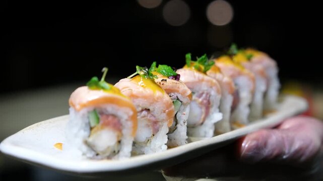 Static close up of a colorful and appetizing sushi platter featuring premium seared salmon rolls with specialty glazes and fresh garnishes on a white ceramic plate with a blurred restaurant background