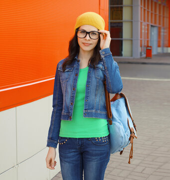 Happy woman student with eyeglasses, backpack standing in the city