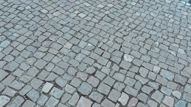 POV tracking shot moving over an ancient cobblestone pavement. Detailed view of gray vintage stones on a historic city street during a walk. High angle perspective of urban ground.