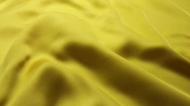 Yellow natural silk fabric waving in the wind. Abstract background of flowing waves and smooth texture. Solid bright golden color with no patterns or prints. 