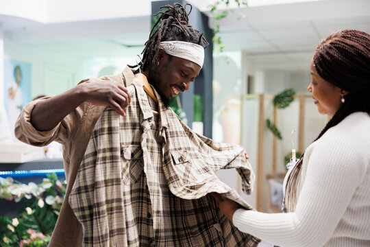 African american man holding plaid shirt to body, showing to wife and asking for advice in clothing store. Couple shopping and trying on casual apparel in fashion boutique