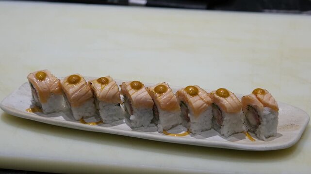 Cinematic tracking shot along a row of perfectly prepared salmon and avocado uramaki sushi rolls on a minimalist white plate with professional garnishes in a high-end Japanese restaurant showing the p