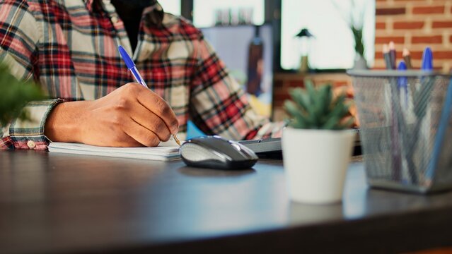 Employee working from home cross referencing information, transcribing data from computer to notebook. Teleworker remotely working in warm cozy stylish home, typing and writing, close up