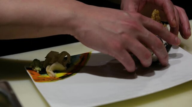 Detailed shot of a professional sushi chef's hands efficiently arranging individual sushi pieces on a white service plate for immediate presentation and hospitality service in a busy restaurant
