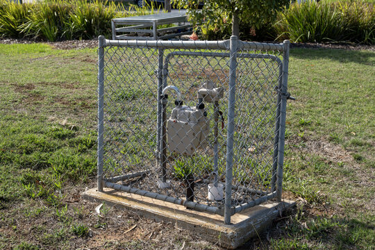 Steel chainlink mesh cage enclosure protecting a water meter or utility valve and pipework infrastructure in a suburban park in Australia, to secure, protect and restrict unauthorised access 