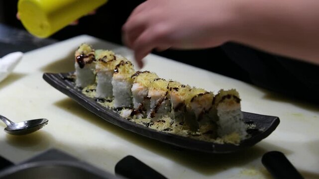 Chef's hands adding final toppings or garnishes to a row of sushi rolls on a professional serving plate for gourmet food presentation and high-end restaurant b-roll